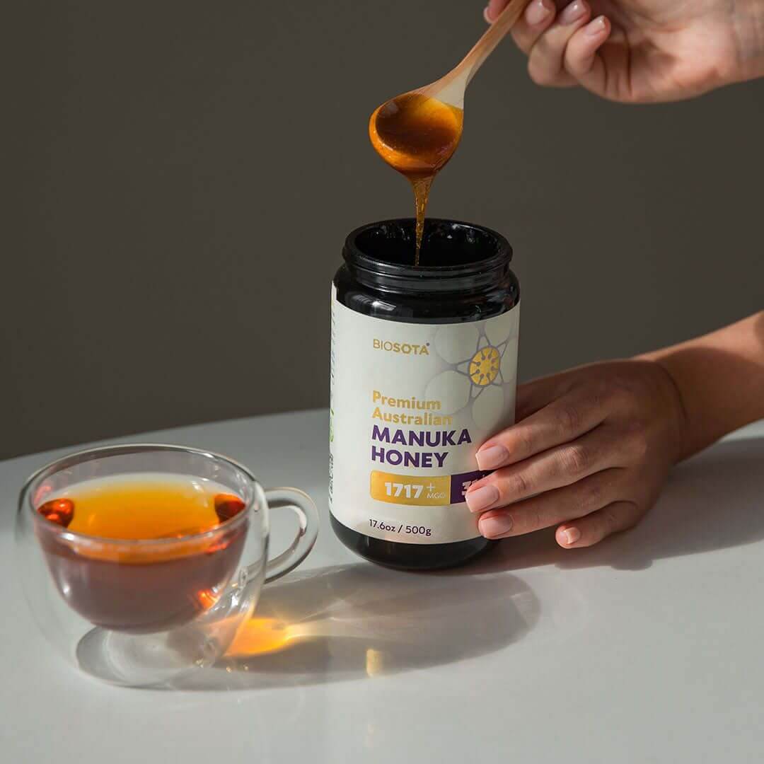 紅茶のカップのそばで、瓶からBiosota Manukaハニーをスプーンですくう情景